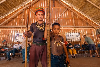 Na foto o cacique Gilvan é um indígena que segura uma lança e está ao lado do filho, uma criança vestida com calça jeans e sem camisa